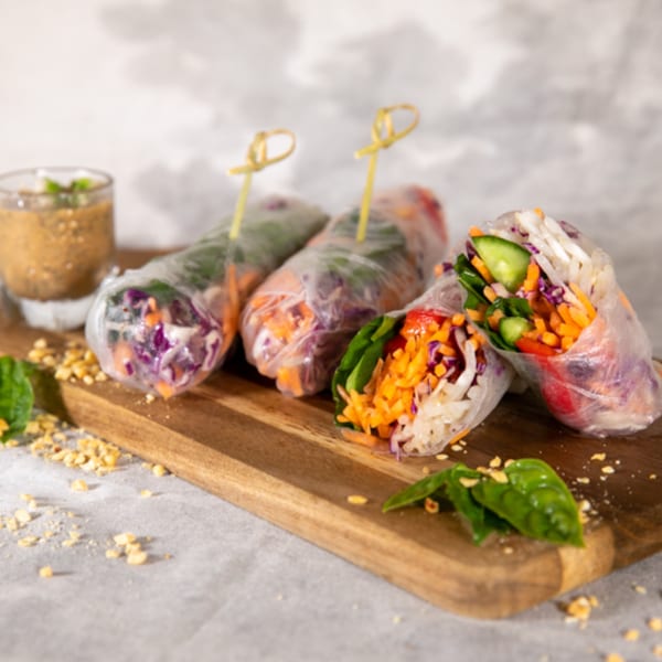 Vegan spring rolls with colorful vegetables and peanut sauce on a wooden board.
