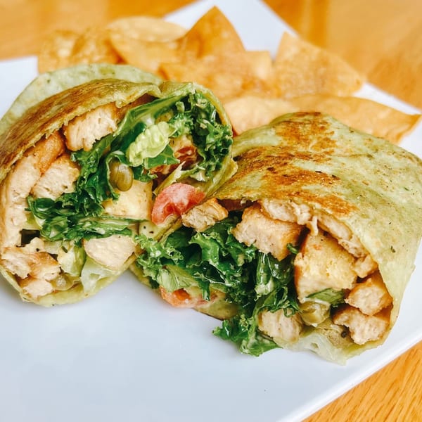 A vegan chicken Caesar wrap, cut in half, with lettuce, tomatoes, and tortilla chips.