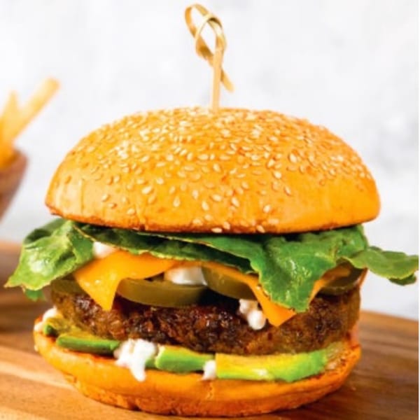 Higher Taste vegan burger with a plant-based patty, cheese, lettuce, avocado, and sauce on a sesame bun.