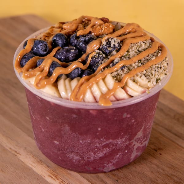 Higher Taste vegan acai bowl with blueberries, bananas, granola, hemp seeds, and peanut butter drizzle.