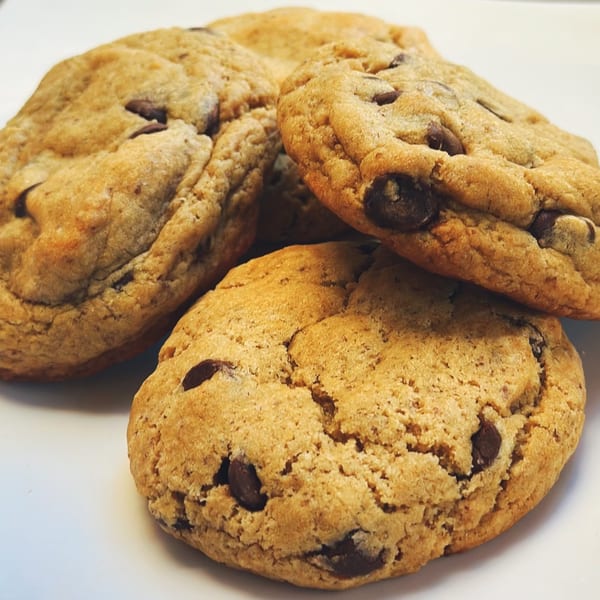 Close-up of three golden-brown vegan chocolate chip cookies on a white surface.